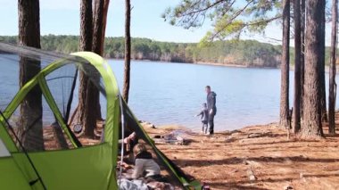 Mutlu bir aile, orman gölünün kıyısında çadır ve şenlik ateşiyle kamp tatilinin tadını çıkarıyor.