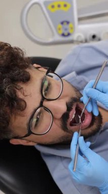 Ağzı açık bir erkek hasta profesyonel aletlerle dişçi muayenesi yaptırıyor.