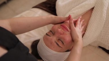 Profesyonel masöz güzellik merkezinde genç bir kadına canlandırıcı yüz masajı yapıyor.