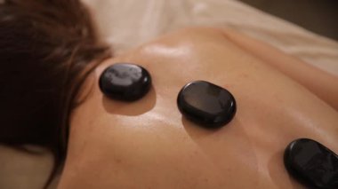 Genç bir kadın lüks bir spa ve sağlık merkezinde sıcak taş terapi seansı sırasında dinleniyor.