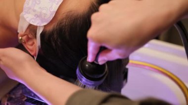 Profesyonel kuaför müşterilerini uzun siyah saçlarıyla kuaför lavabosunda duş başlığıyla yıkıyor.