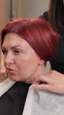 Profesyonel kuaför, saçını kesmeden önce kızıl saçlı bir kadının etrafına koruyucu pelerin takıyor.