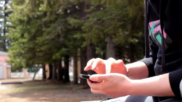어린 소녀는 공원에서 벤치에 앉아있는 동안 스마트폰 사용 하 여 — 비디오