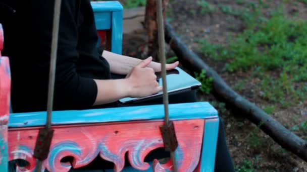 Menina com o tablet em um balanço de madeira mãos — Vídeo de Stock