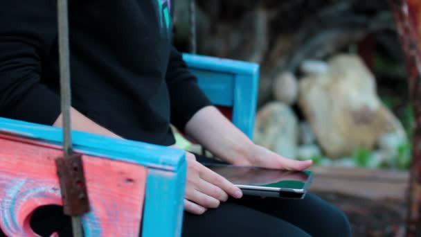 Fille avec la tablette sur une balançoire en bois mains — Video