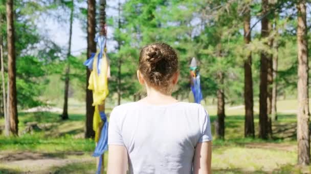Дівчина проходить через ритуальні ворота з різнокольоровими стрічками в лісі. шаманізму — стокове відео