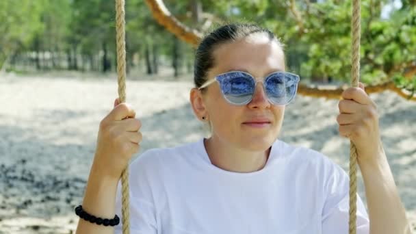 Portræt af en pige i solbriller sidder på et reb swing – Stock-video