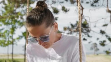 Rahatlamış genç bir kadın halat üzerinde salıncak akıllı telefon kullanıyor.