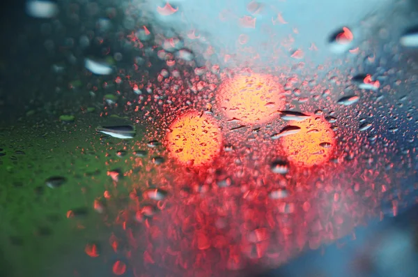 Bokeh of a red lights of rear car, looking through a wet window — Stock Photo, Image