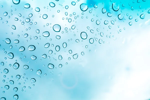 Su arka plan damla. Su cam pencere üzerinde üzerinde mavi gökyüzü düşüyor.