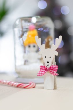Ahşap bir ren geyiği heykelciği ve şenlik ayrıntılarıyla küçük bir kar küresinin yer aldığı el yapımı şirin bir Noel süsü. Sıcak kış tatili atmosferi, arka planda hafif ışıklar mevsimlik dekorlar ve hikaye anlatımları için mükemmel..