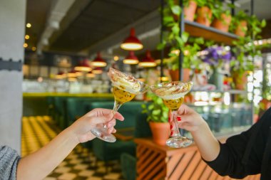 Uzun martini bardaklarında iki porsiyon çikolatalı tatlı. İki genç kadın ellerinde tatlı bardaklarıyla restoranın arka planında bulanık, seçici bir odak noktası var. Şerefe, arkadaşlarla boş zaman..