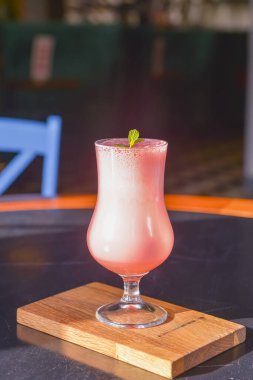 Lokantadaki siyah ahşap bir masada servis edilen uzun bir lale bardağındaki pembe meyve kokteyli. Seçici odaklanma, bulanık arkaplan. Nefis ferahlatıcı alkol içeceği..