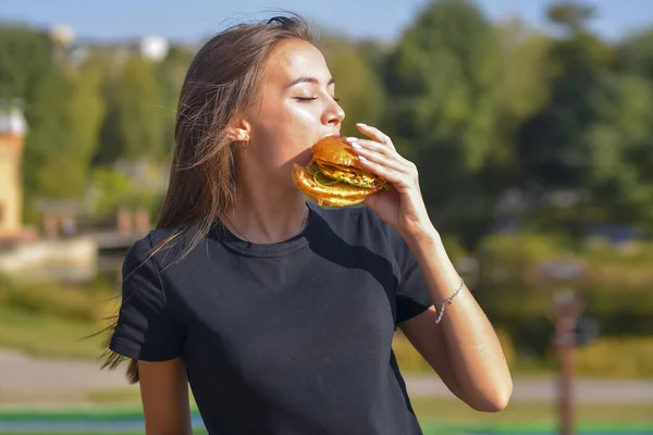 Hamburger yiyen ve patates kızartması yiyen bir kadın. Güzel beyaz kadın manken elleri dışarıda bulanık bir şekilde hamburger yiyor. Hayat, dışarıda yemek kavramı..