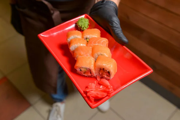茶色のレンガの背景に対して 寿司のプレートとウェイター レストランサービス 仕事でウェイター レストランで外食する 日本料理 — ストック写真