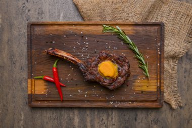 Ahşap arka planda, ahşap bir tahtanın üzerinde servis edilen baharatlı baltalı ızgara biftek. Mangal konsepti, ızgara biftek, sonbahar yemekleri..