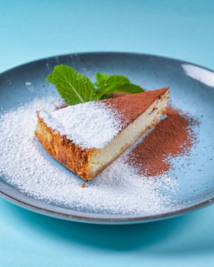 Mavi arka planda New York peynirli keki dilimi. Bir parça peynirli kek, şeker, kakao tozu ve bir parça et..