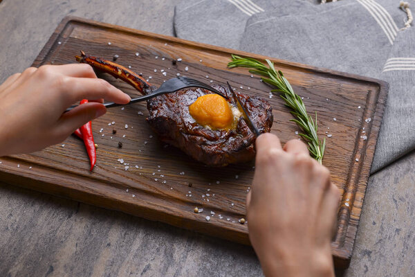 Barbecue tomahawk steak with spices served on a rustic wooden board over wooden background. BBQ concept, grilled meat steak, autumn seasonal dish. Eating steak with knife and fork.