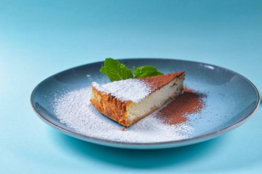 Mavi arka planda New York peynirli keki dilimi. Bir parça peynirli kek, şeker, kakao tozu ve bir parça et..