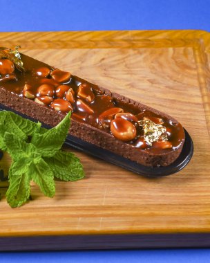 Kahverengi çikolatalı tatlı, fındıklı ve karamelli. Kırsal ahşap bir tahta üzerinde servis edilmiş. Üzerinde de nane yaprakları var. Çay ya da kahve saati için lezzetli tatlı pasta..