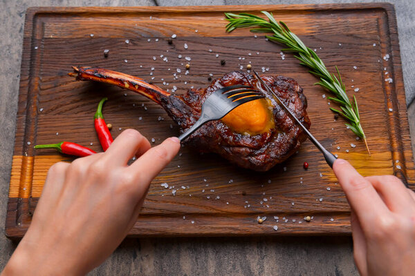 Barbecue tomahawk steak with spices served on a rustic wooden board over wooden background. BBQ concept, grilled meat steak, autumn seasonal dish.