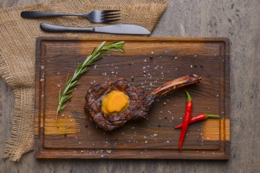 Ahşap arka planda, ahşap bir tahtanın üzerinde servis edilen baharatlı baltalı ızgara biftek. Mangal konsepti, ızgara biftek, sonbahar yemekleri..