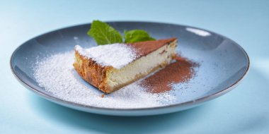 Mavi arka planda New York peynirli keki dilimi. Bir parça peynirli kek, şeker, kakao tozu ve bir parça et..