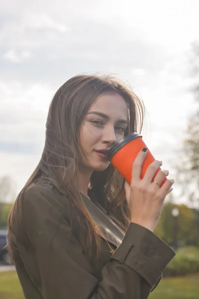 Young attractive woman with a cup of coffee to go. Drinking coffee outside in autumn clothes during fall season. Coffee time.