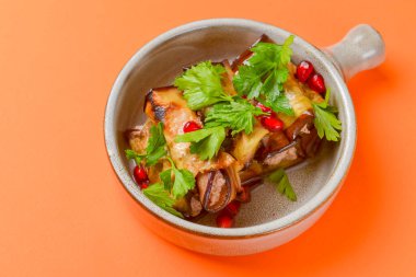 Turuncu arka planda servis edilen bir kasede et ve nar tohumlu patlıcan ruloları. Gürcistan mutfağı kavramı.