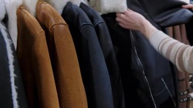 Elbise mağazasında askıda asılı kürk yakalı, farklı renkte deri ceket seçen bir kadına yaklaş.