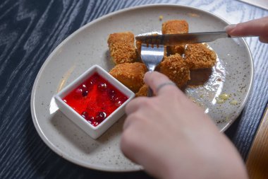 Kızarmış camembert peyniri ve kızılcık sosu beyaz tabakta servis ediliyor. Çatal ve bıçakla peynir yemek. Sakin bir hayat, restoran konseptinde yemek yemek..