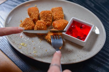 Kızarmış camembert peyniri ve kızılcık sosu beyaz tabakta servis ediliyor. Çatal ve bıçakla peynir yemek. Sakin bir hayat, restoran konseptinde yemek yemek..