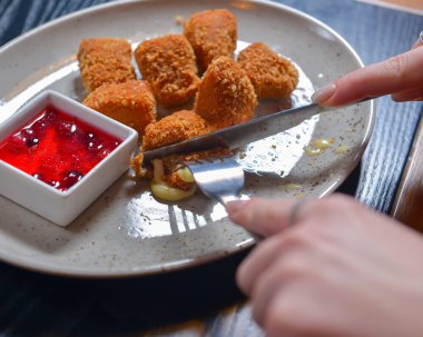 Kızarmış camembert peyniri ve kızılcık sosu beyaz tabakta servis ediliyor. Çatal ve bıçakla peynir yemek. Sakin bir hayat, restoran konseptinde yemek yemek..