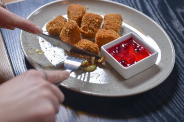 Kızarmış camembert peyniri ve kızılcık sosu beyaz tabakta servis ediliyor. Çatal ve bıçakla peynir yemek. Sakin bir hayat, restoran konseptinde yemek yemek..