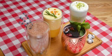 Farklı bardaklarda çeşitli süt menüleri için. Soğuk sonbahar ya da kış havası için Hor içkileri, sonbahar mevsimi. Meyve çayı, kakao içeceği, kibrit latte, kırmızı ekose masa örtüsü üzerine hurma çayı..