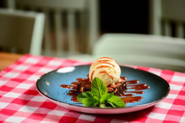 Kırmızı ekose masa örtüsüyle mavi bir tabakta servis edilen geleneksel dondurmalı browni tarifi. İtalyan mutfağı konsepti, tatlı tatlı. Kapat..