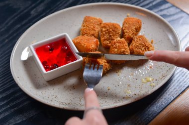 Kızarmış camembert peyniri ve kızılcık sosu beyaz tabakta servis ediliyor. Çatal ve bıçakla peynir yemek. Sakin bir hayat, restoran konseptinde yemek yemek..