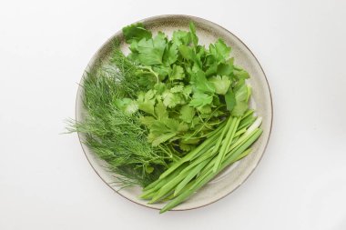 Taze otlar, soğan, dereotlu ve maydanozlu beyaz arka planda. Tabakta sağlıklı taze yeşillik.