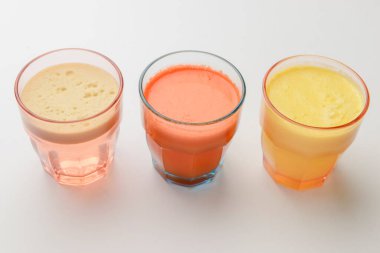 İzole edilmiş narenciye suyu. Beyaz zemin üzerinde portakal, greyfurt ve limon suyu bulunan üç bardak. Beyaz, küçük bardaklarda taze, sağlıklı bir içecek..