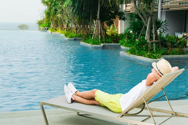 Chaise longue and swimming-pool. Boy on the longue chair near the swimming pool relaxing. Travel concept, travelling, hotel business. Rest, sleep time, relax. Copy space banner.