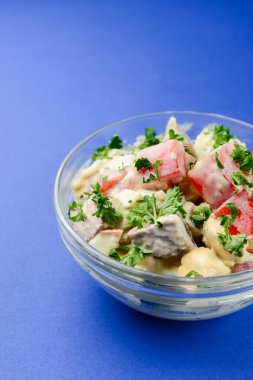 Bir kase sebze salatası, ızgara meta, domates, mantar. Kasede mayonez salatası. Mavi arka planda bir akşam yemeği fikri.