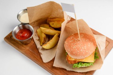 Patates ve soslu hamburger. Tahta tahtada beyaz arka planda sulu bir burger. Fast food, abur cubur konsepti. Amerikan tarzı.