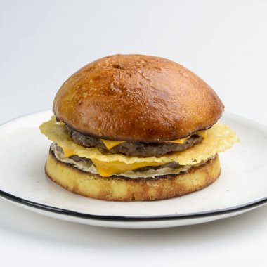 Beyaz arka planda beyaz bir tabakta servis edilen jambonlu ve peynirli dev gibi mükemmel bir hamburger. Kapatın. Fast food, abur cubur kavramı.