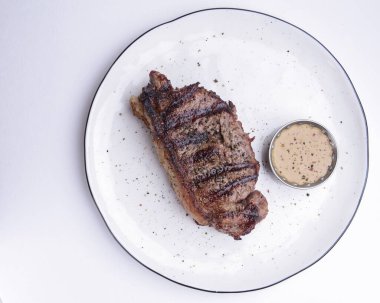 Beyaz arka planda beyaz bir tabakta servis edilen soslu leziz biftek. Barbekü eti, barbekü konsepti. Lezzetli yemek fikri..