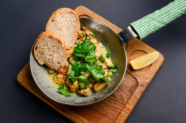 Siyah arka planda kızarmış ekmek ile servis edilen tavada sarımsak ve fesleğenli enfes taze istiridye. Akşam yemeği için yemek. Üst görünüm.