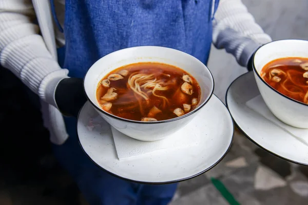 Bowl of Chinese noodle soup with chicken broth and mushrooms. Served by waiter in restaurant or diner. Eating out concept, waiter at work, idea for a dinner.