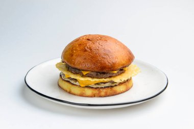 Beyaz arka planda beyaz bir tabakta servis edilen jambonlu ve peynirli dev gibi mükemmel bir hamburger. Kapatın. Fast food, abur cubur kavramı.