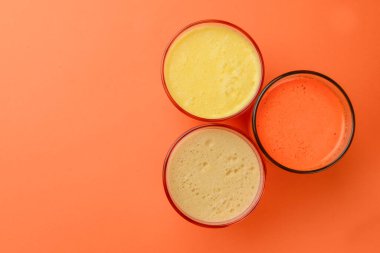 Isolated citrus juice. Three glasses with orange, grapefruit and lemon juice isolated on orange background. Fresh healthy drink on white, small glasses.