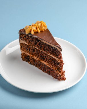 Piece of chocolate cake with icing on blue background. Sweet dessert for tea or coffee time. Close up.