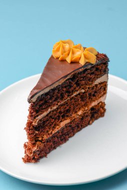 Piece of chocolate cake with icing on blue background. Sweet dessert for tea or coffee time. Close up.